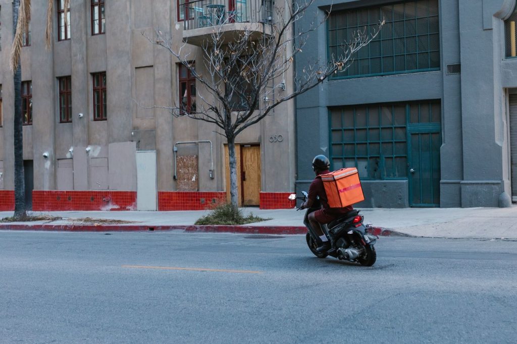 Entregador em motocicleta circula por uma área urbana durante o trabalho.